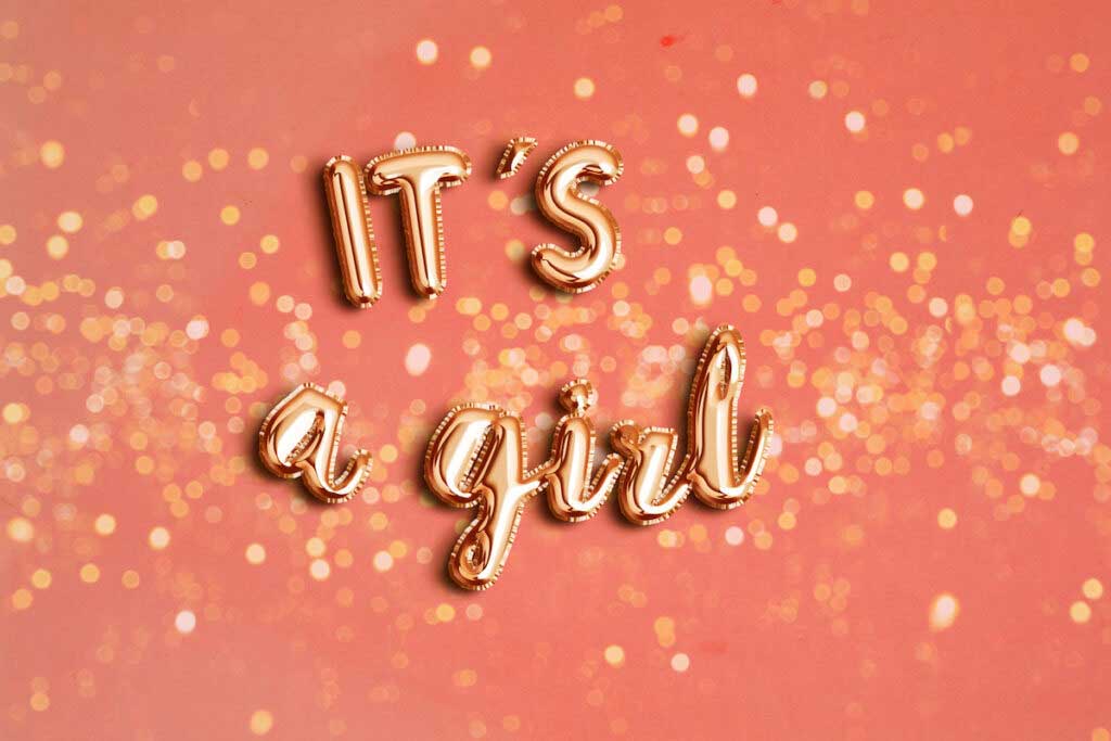 Gold balloons spell out "It's a girl" on a pink background.