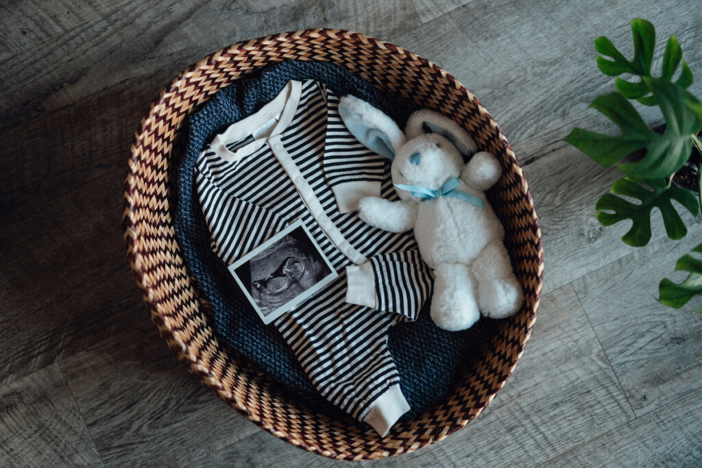 A baby basket with onsie, stuffed rabbit, and sonogram picture waits ready for a baby.