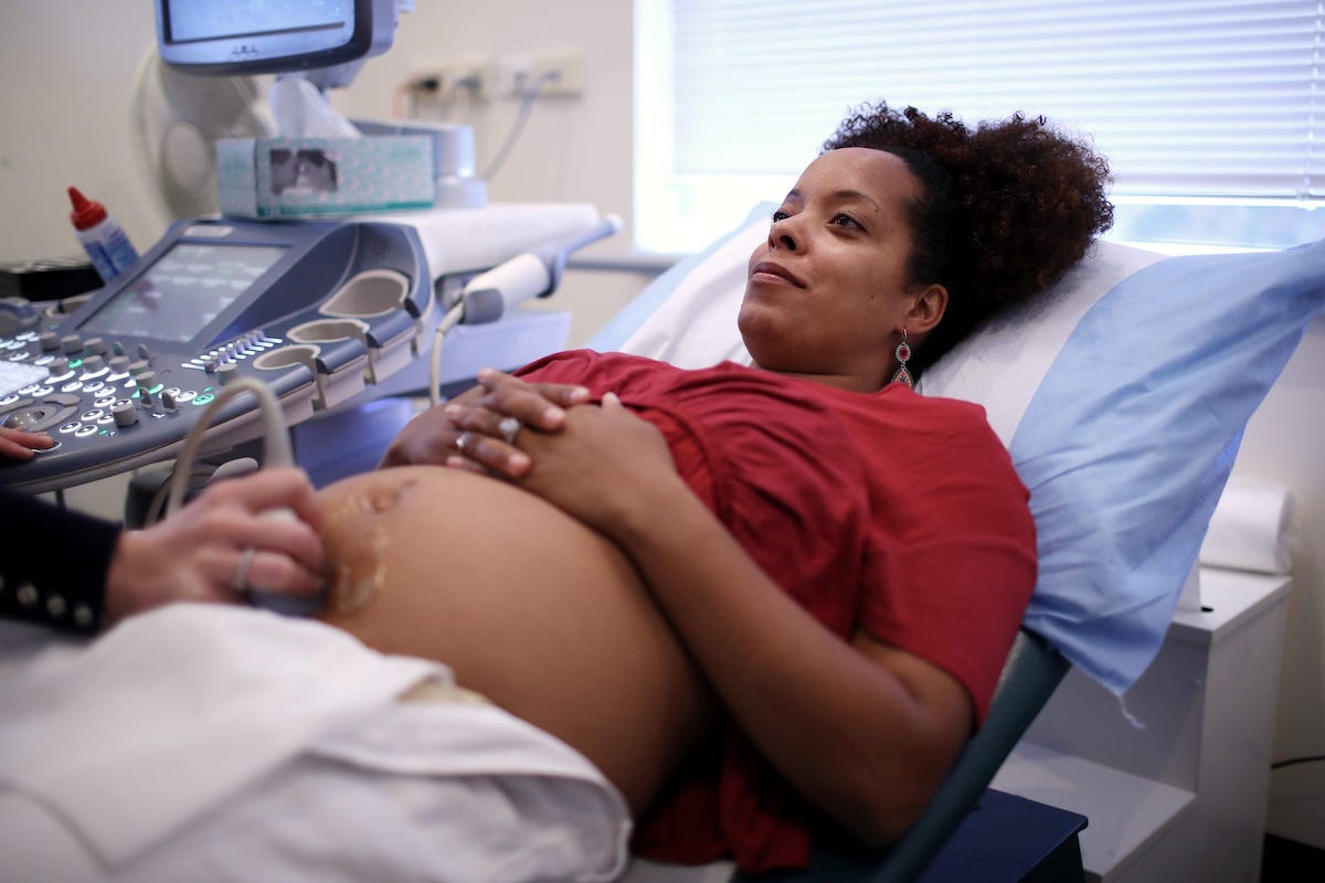 A Black mother reclines on an exam table while having an ultrasound.