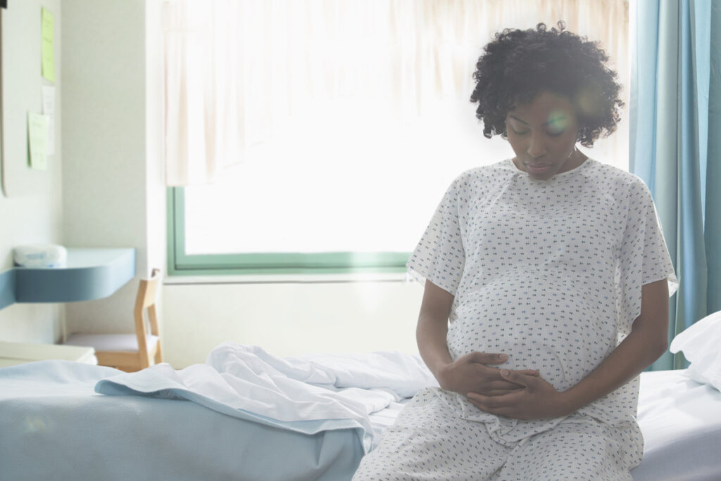 A Black pregnant woman rests her hands on her stomach while waiting for a doctor's appointment.
