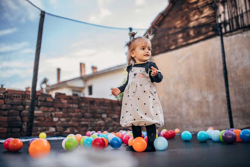 A baby plays on a trampoline filled with plastic balls.