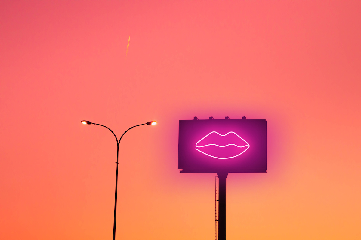 A billboard with hot pink lips glows against a sunset.