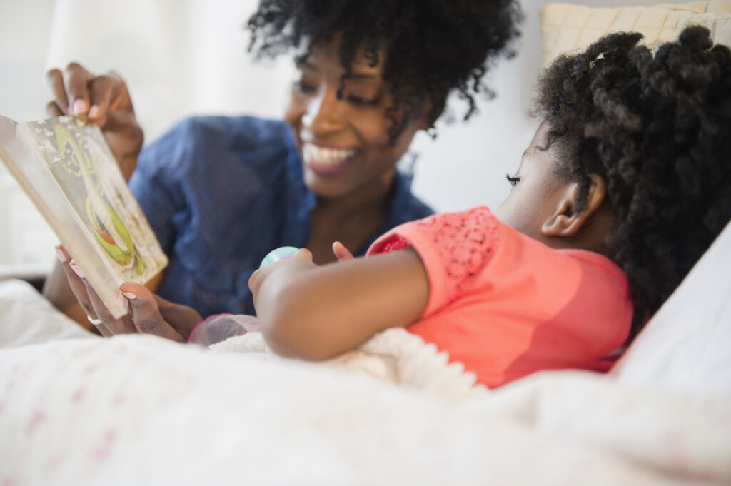Mother reads a book to her daughter in bed.