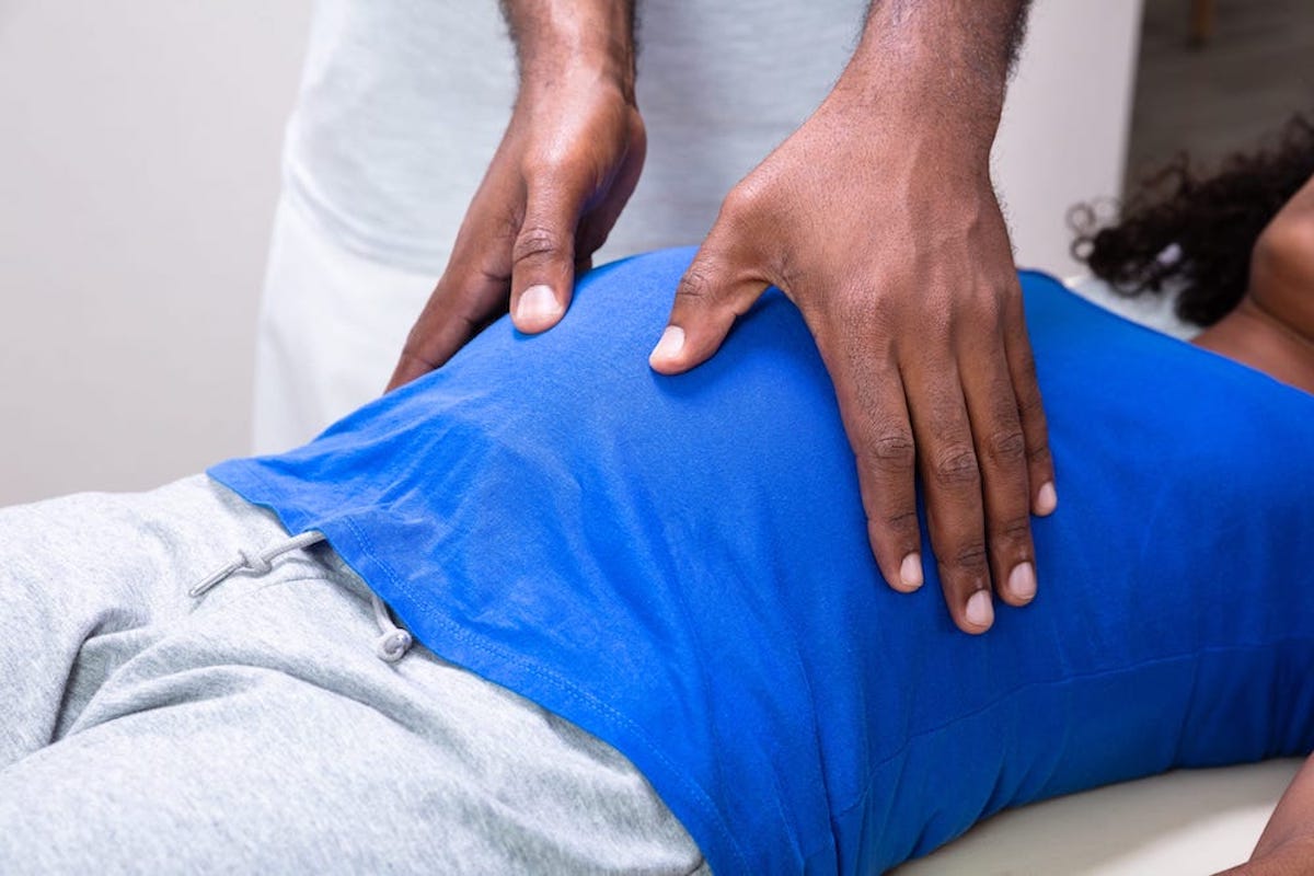 A pregnant woman lies on her back while a doctor stands over her with his hands on either side of her belly.