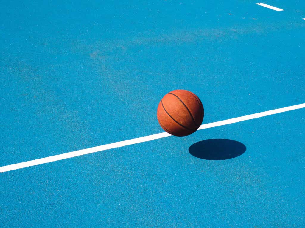 A bright orange basketball bounces across a teal court.