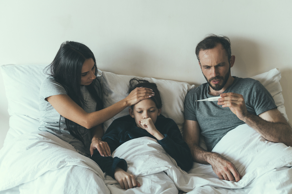 Two parents, in bed with their child, who is coughing, take the child's temperature.