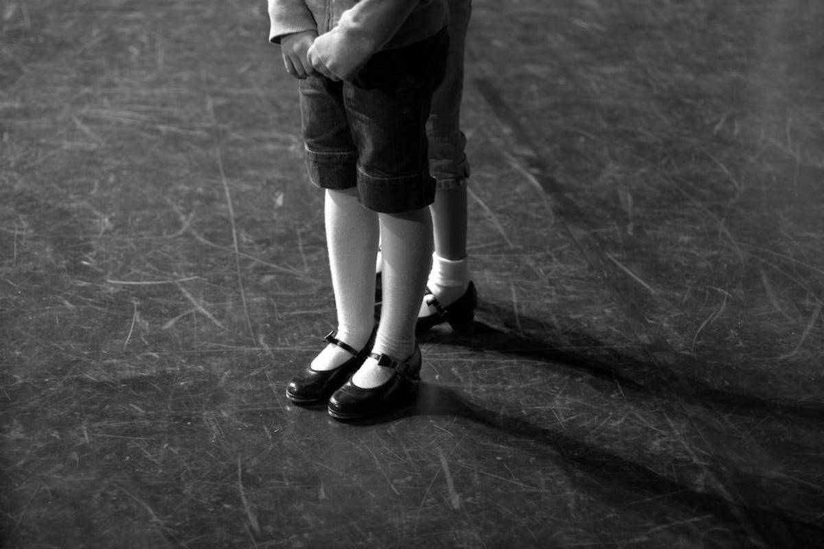 Two children wearing tap shoes are seen from the knees down.