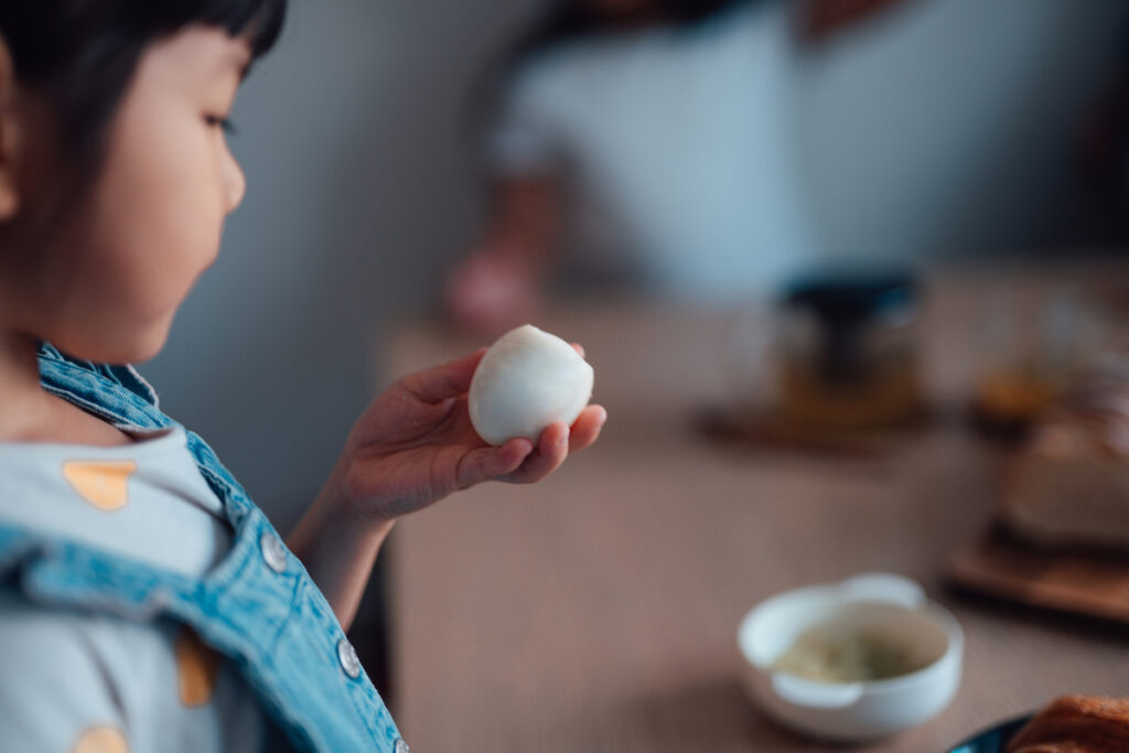 Young child examines a hard-boiled egg at the dinner table.