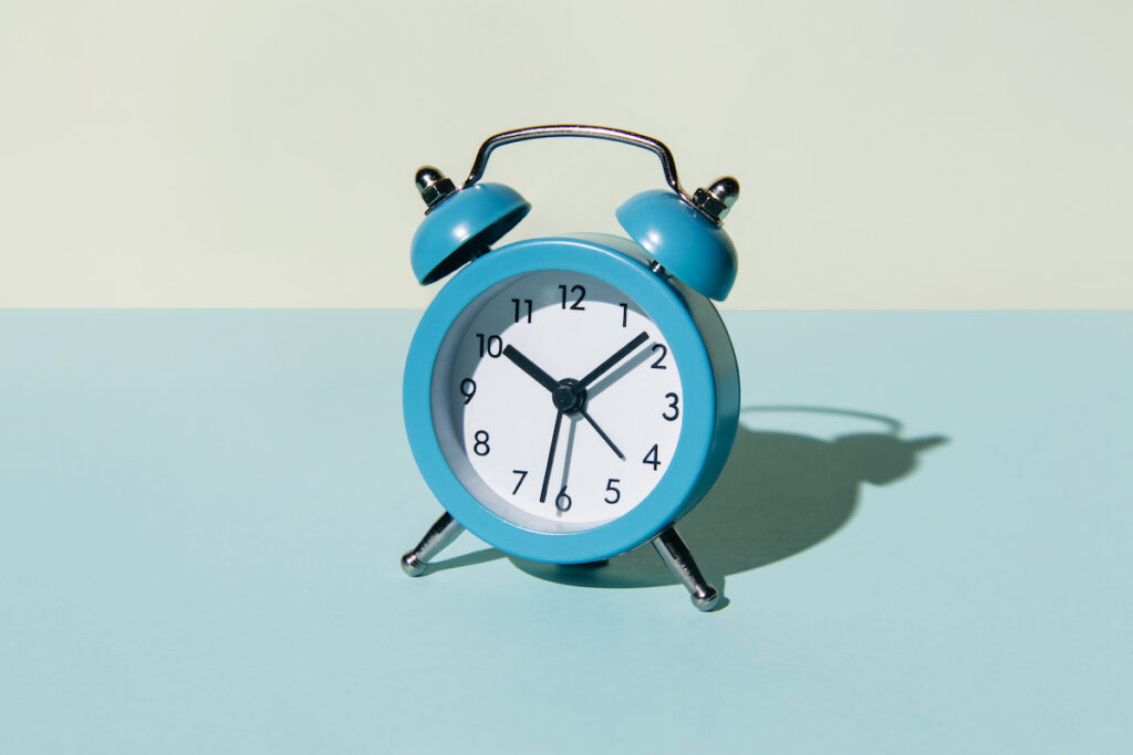 A blue alarm clock with two bells sits on a blue and white background.