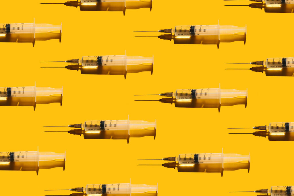 A pattern of yellow syringes with clear liquid on a yellow background.