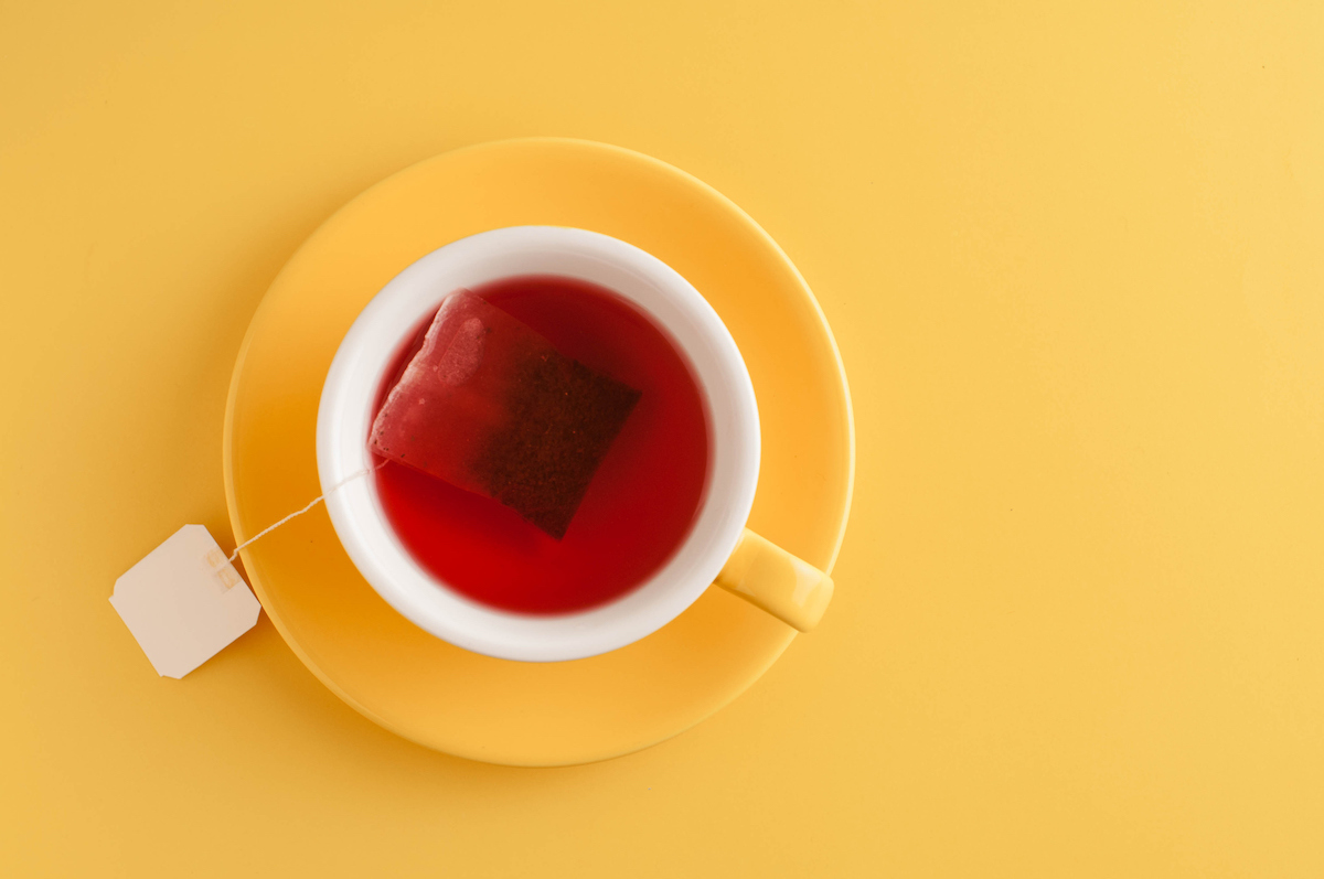 A yellow teacup filled with tea is seen on a yellow background.