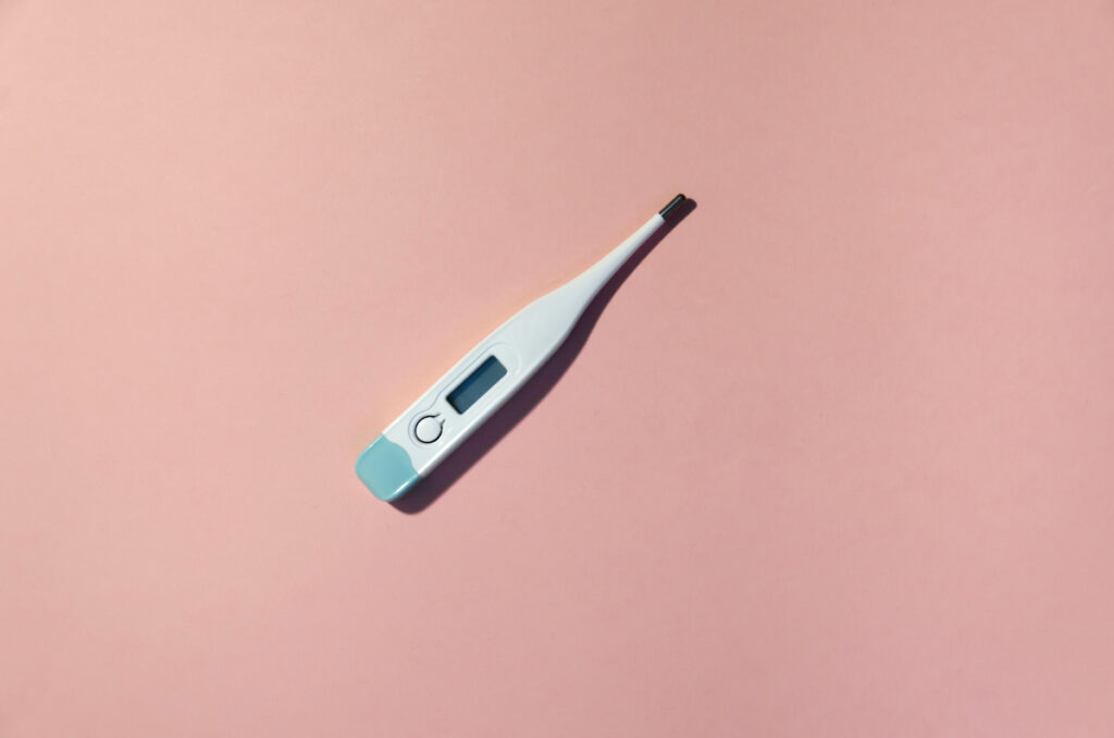 A blue and white digital thermometer sits on a pink background.