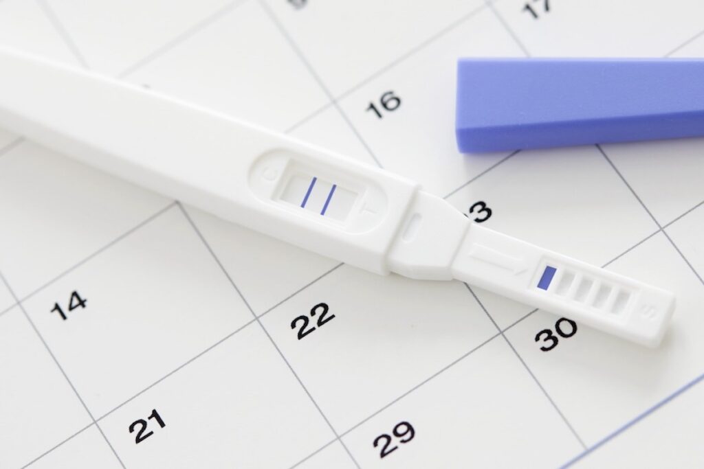 A positive pregnancy test is seen resting on top of a calendar.