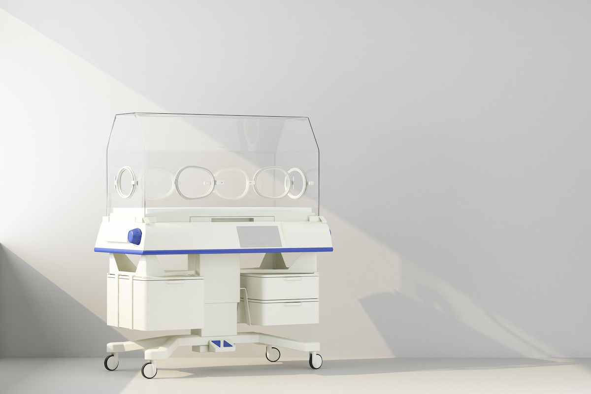 An empty NICU isolette is pictured against a gray wall.