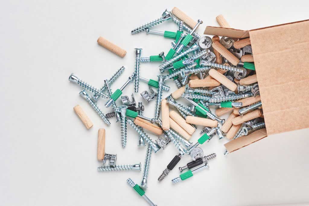 An open box with screws, wood pegs, and anchors for furniture assembly.