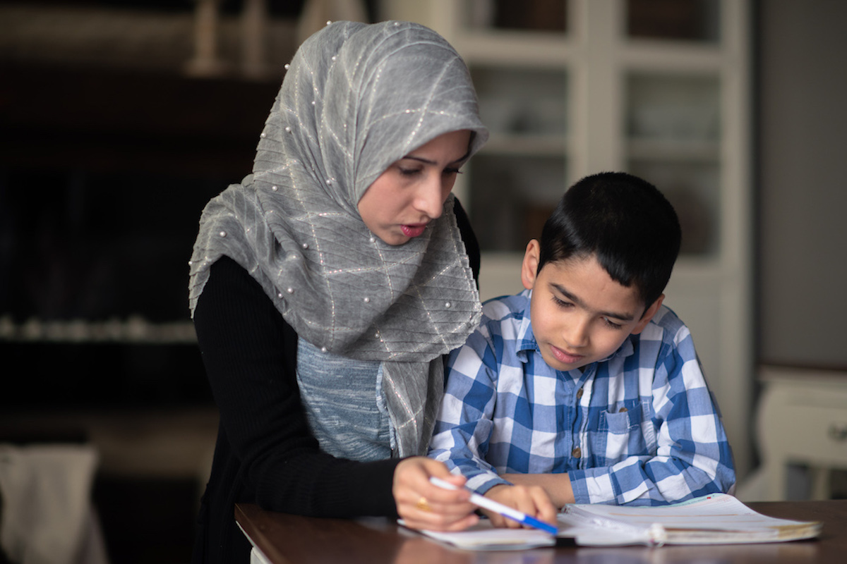 A mother helps her child complete homework at the kitchen table.