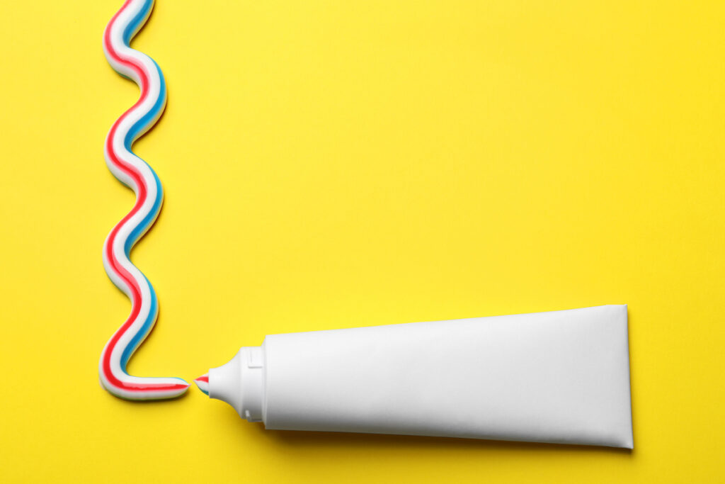 Red, white, and blue striped toothpaste is squeezed into a squiggle on a yellow background.