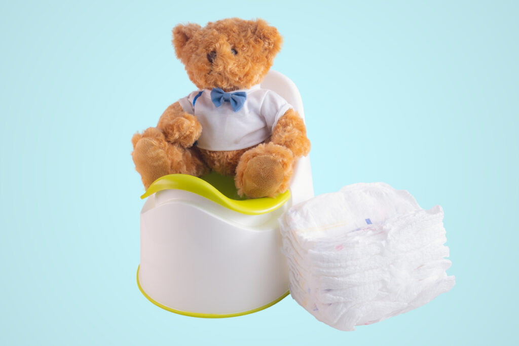 A brown teddy bear sits on top of a plastic potty next to a stack of diapers.