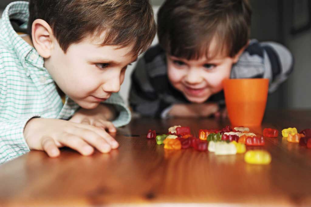 Two kids eye gummy bears piled on a table.