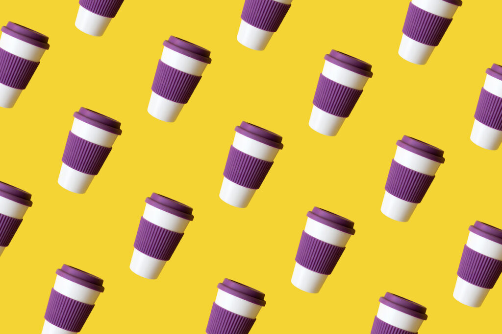 Reusable coffee cups with purple silicone lids and sleeves on a yellow background.