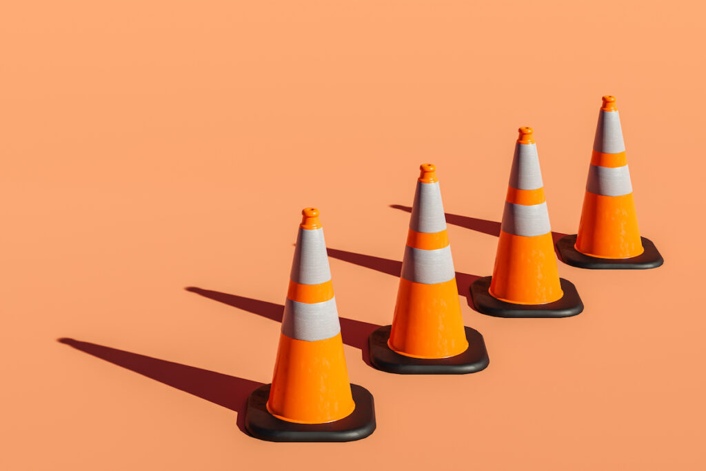 Four orange traffic cones are lined up on a light orange background.