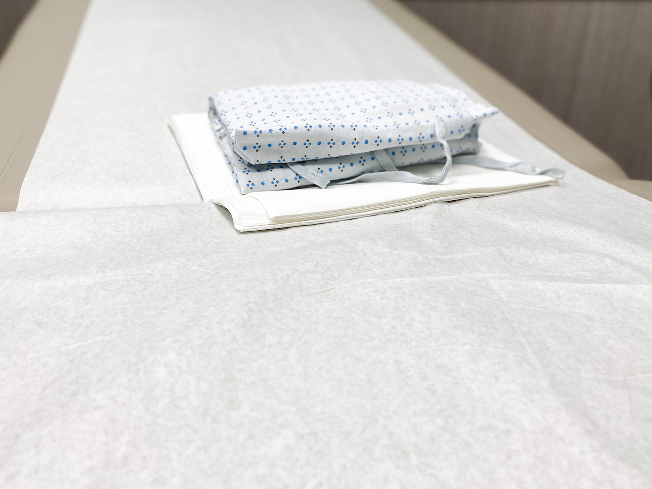 A medical exam table is seen with a folded hospital gown and paper sheet.