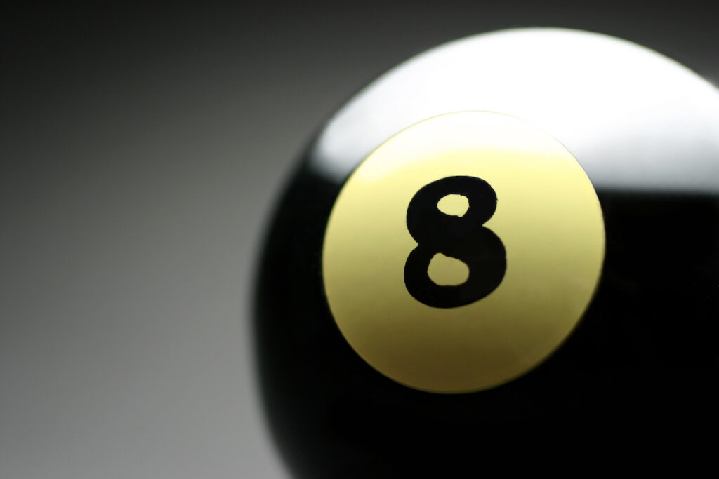 A magic 8 ball is seen on a gray background.