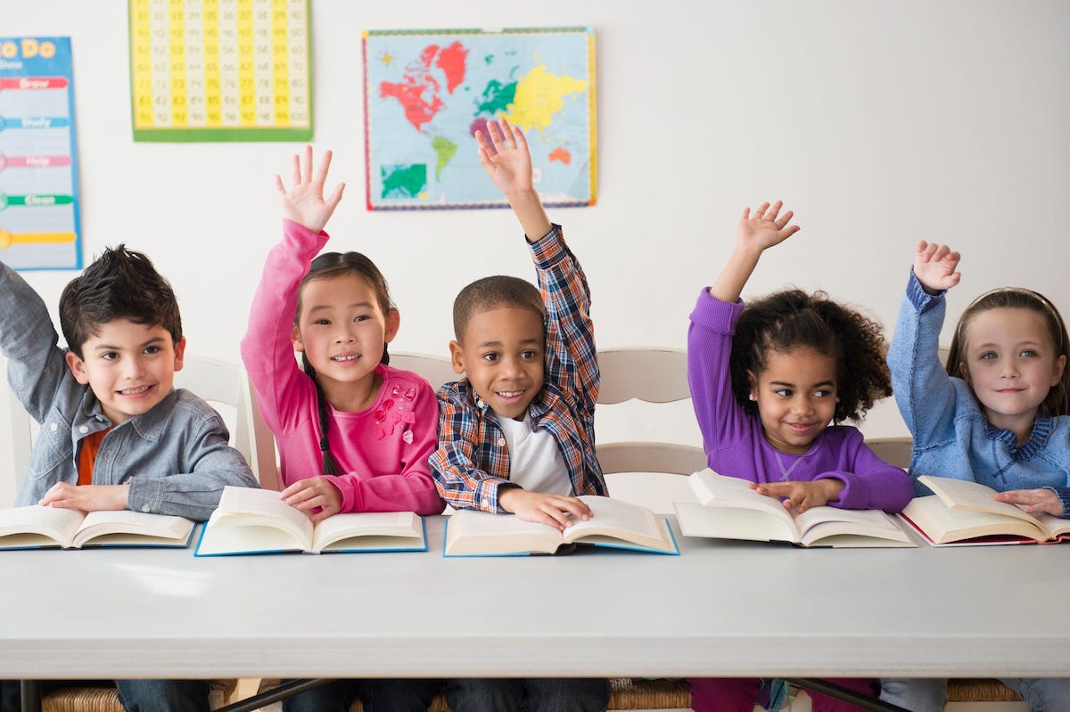 A row of smiling children with books raise their hands.