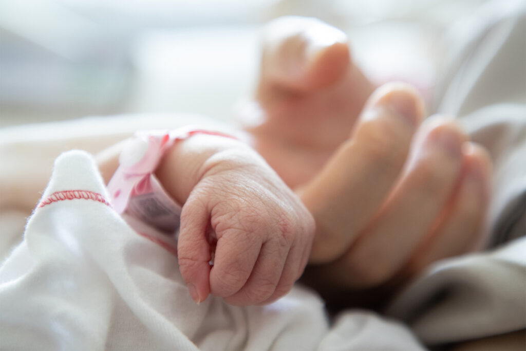 A newborn infant holds the finger of a parent in the hospital.