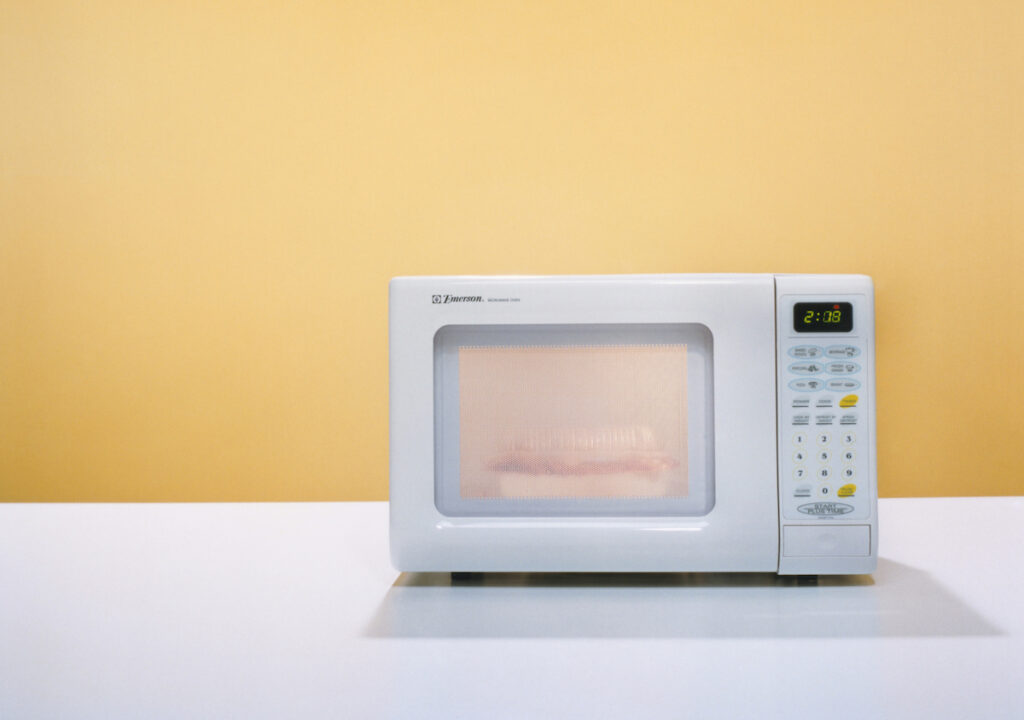 A microwave cooks a meal against a yellow background.