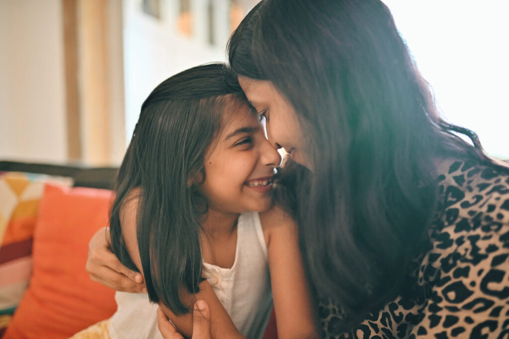 A closeup of a mother and daughter leaning their foreheads together and smiling.