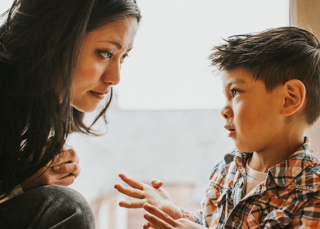 A child looks serious while explaining something to a parent, who is leaning in close.