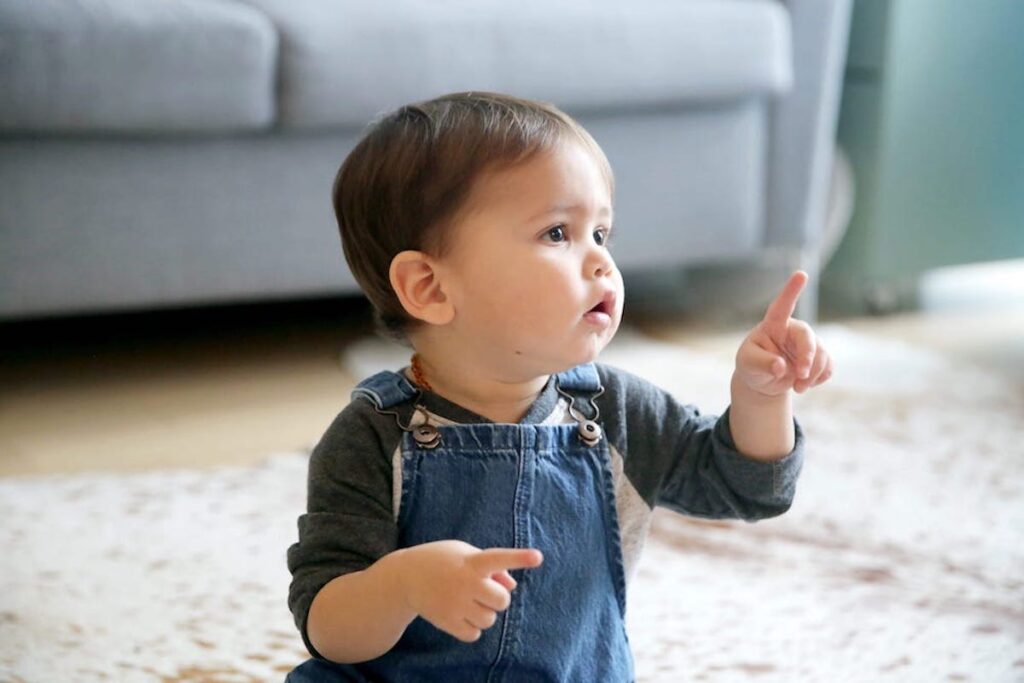 A sitting infant holding up pointer fingers on both hands points to something off-camera.
