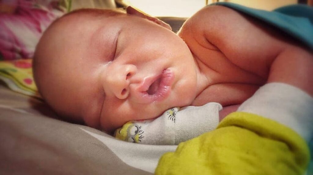 A newborn wears mittens while sleeping.