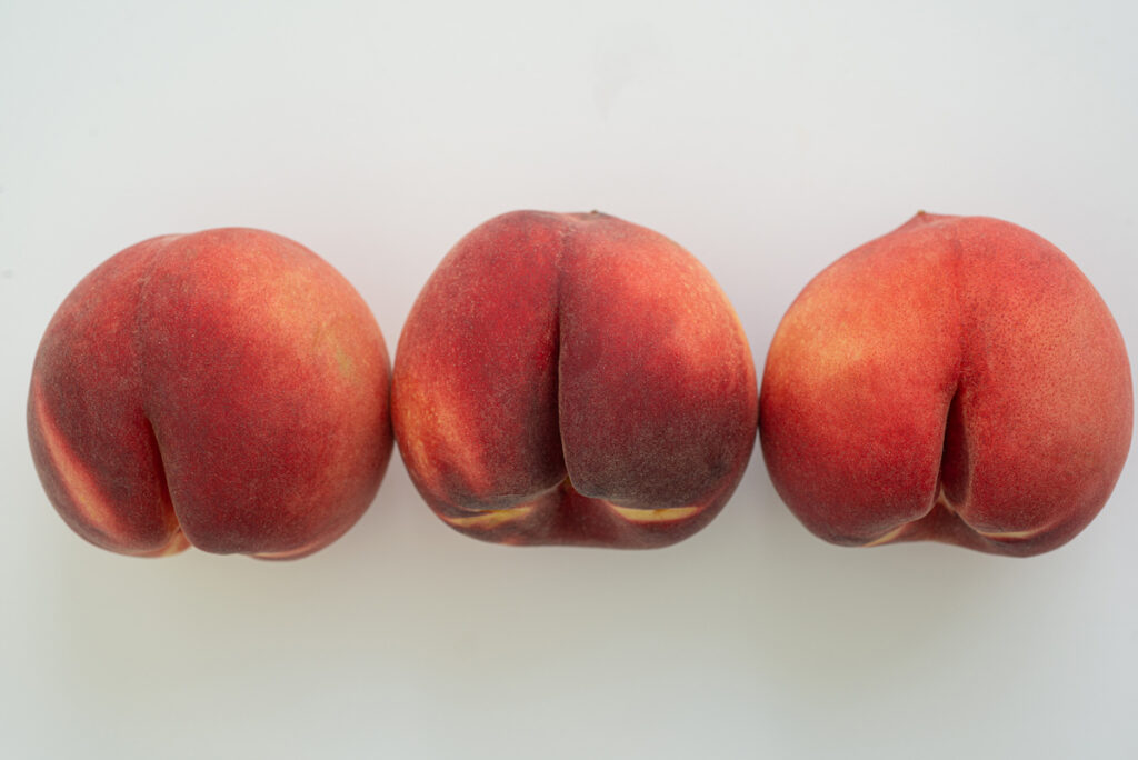 A row of three peaches on a white background that resemble human rear ends.