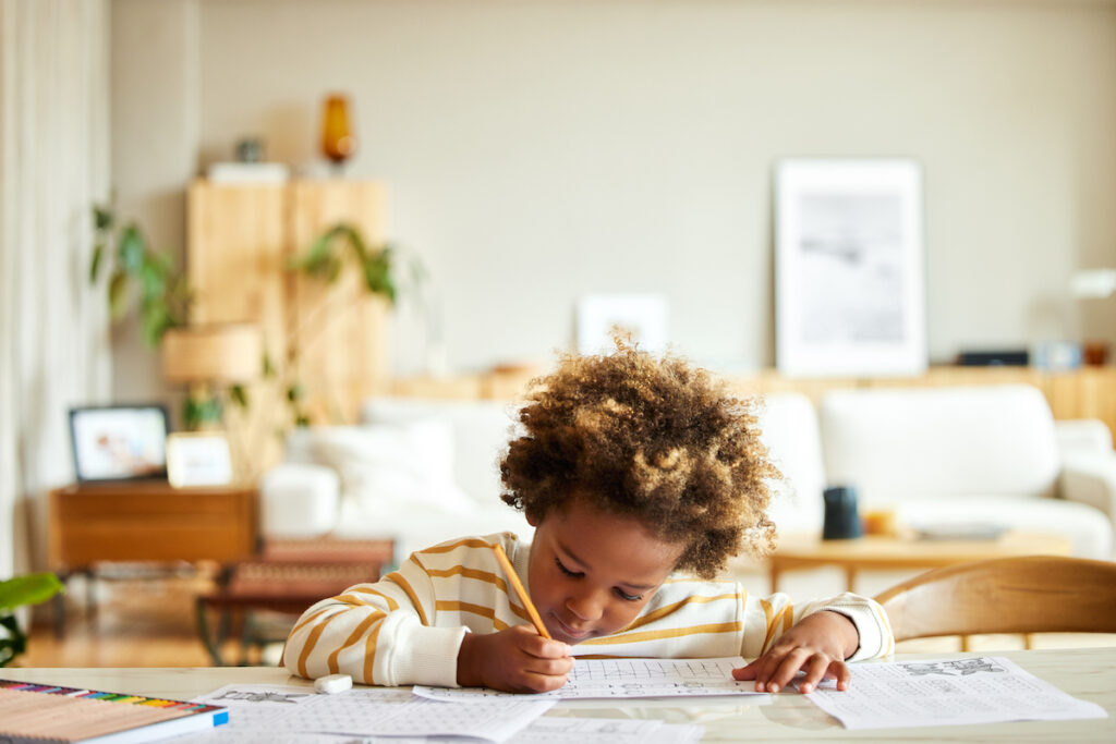 A child with a pencil completes worksheets at a kitchen table.