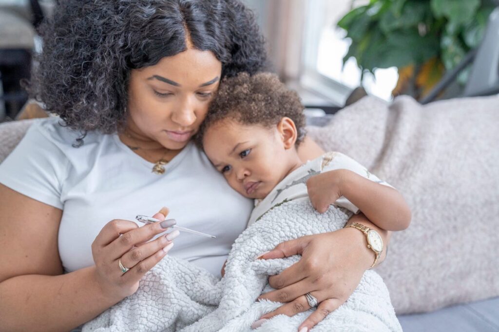 Mother holding a toddler takes her baby's temperature and frowns.