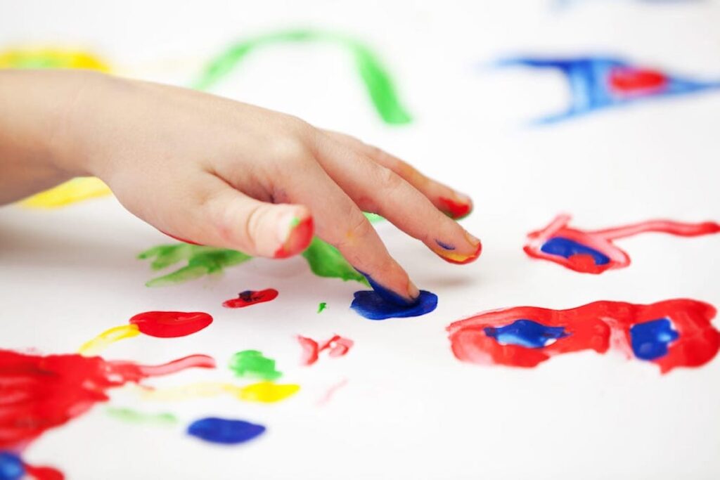 A close up of a child finger painting with brightly colored paints.