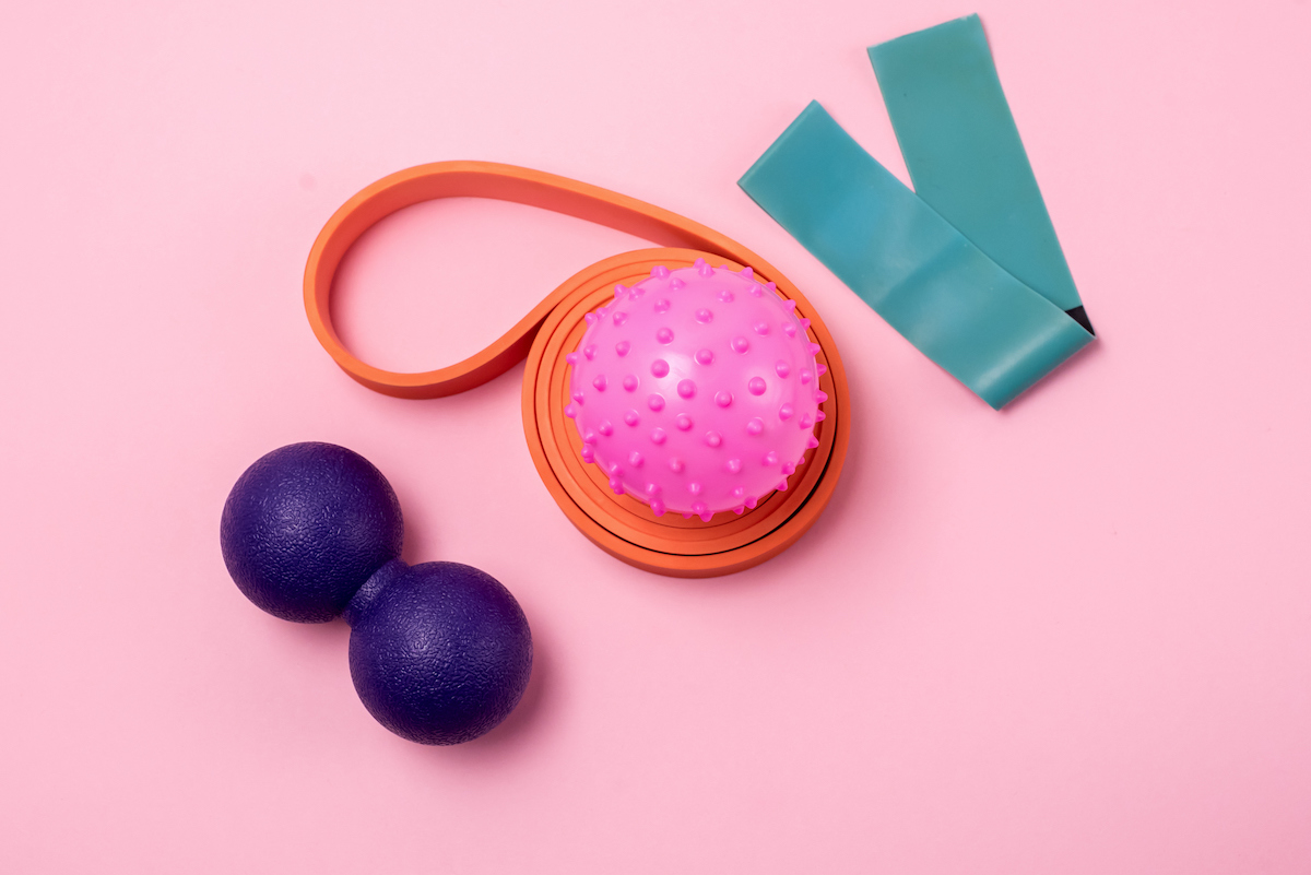 Fitness bands and rollers for stretching on a pink background.