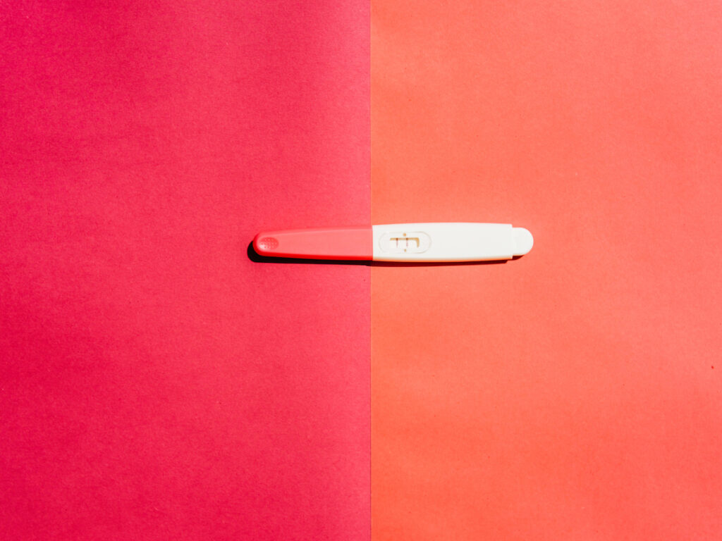 A positive pregnancy test is seen on a pink and orange background.
