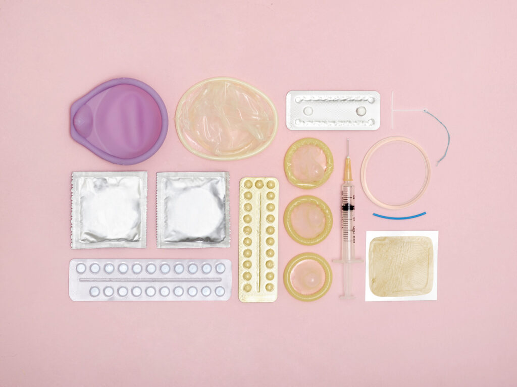 Different types of contraception are laid out on a pink background.