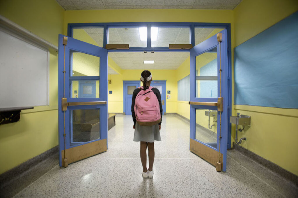 Rear view of a student in a skirt with a pink backpack walking down a yellow school corridor.