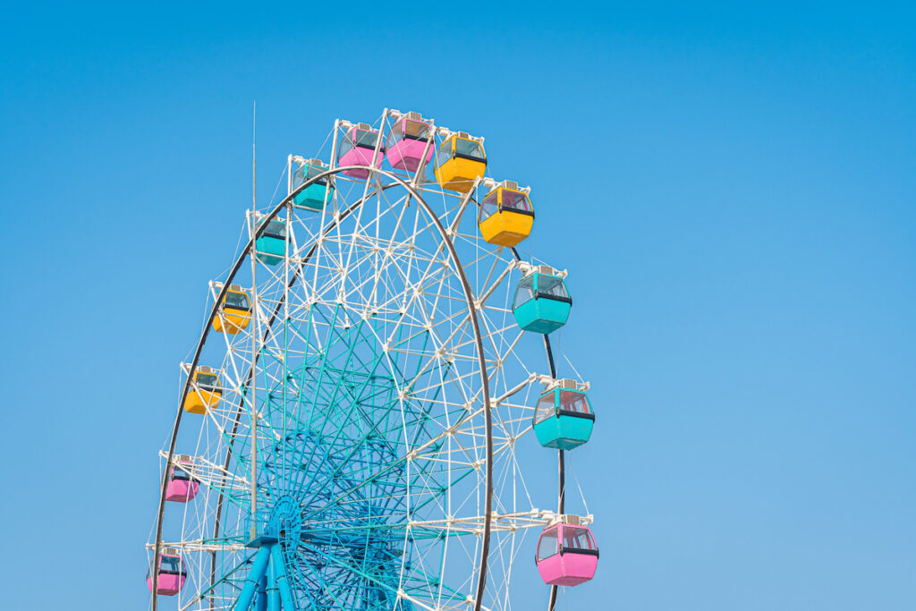 A ferris wheel with pink, yellow, and teal cars against a bright blue sky.