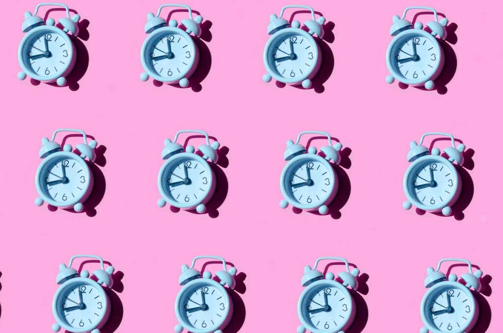 Pattern of light blue alarm clocks arranged across a pink background.