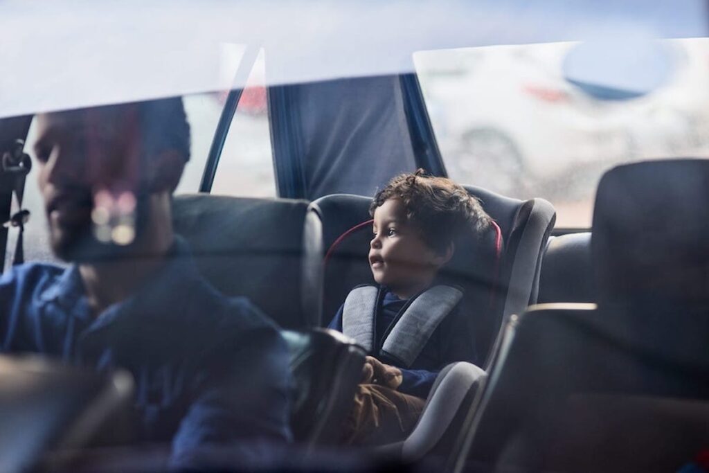 A kid in a carseat looks out the window of a car.