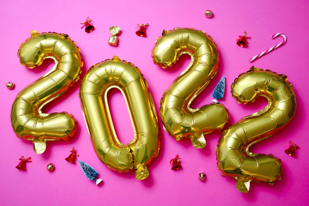 Foil gold balloons spell out "2022" on a pink background.
