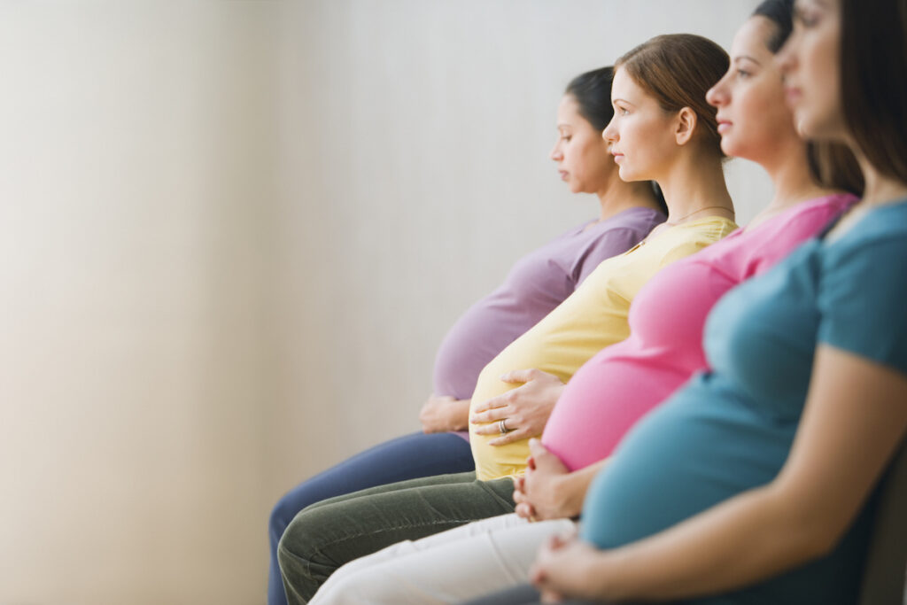 Group of pregnant women sitting in a row in colorful t-shirts.