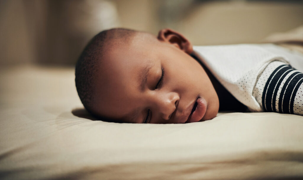 A young boy sleeps on his stomach in bed.