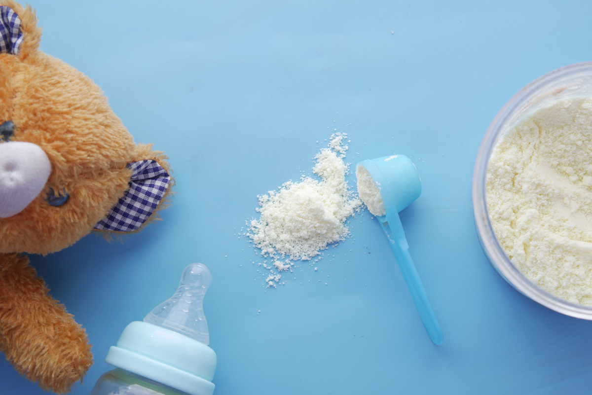 A scoop of baby powder spilled on a blue background next to a teddy bear and empty bottle.