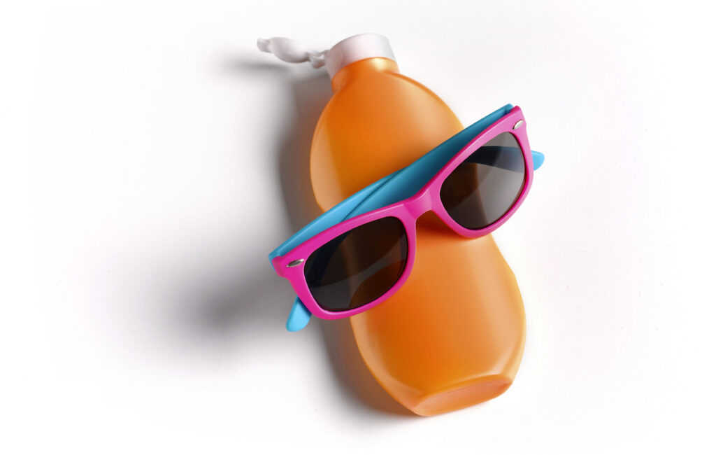 An orange bottle of sunscreen wearing pink and blue children's sunglasses.